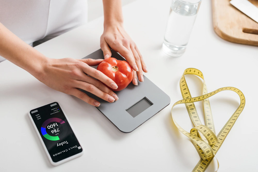 cropped view of woman putting tomato on scales illustrating calorie-counting